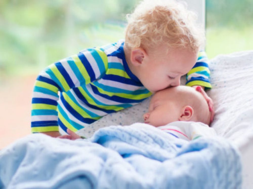 Little boy kissing newborn baby brother